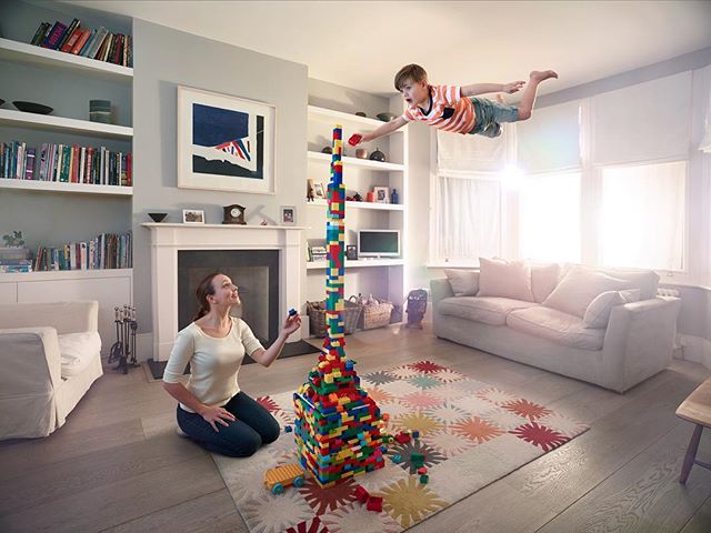 A woman and boy play with blocks in a living room, constructing a tall tower in a playful scene.