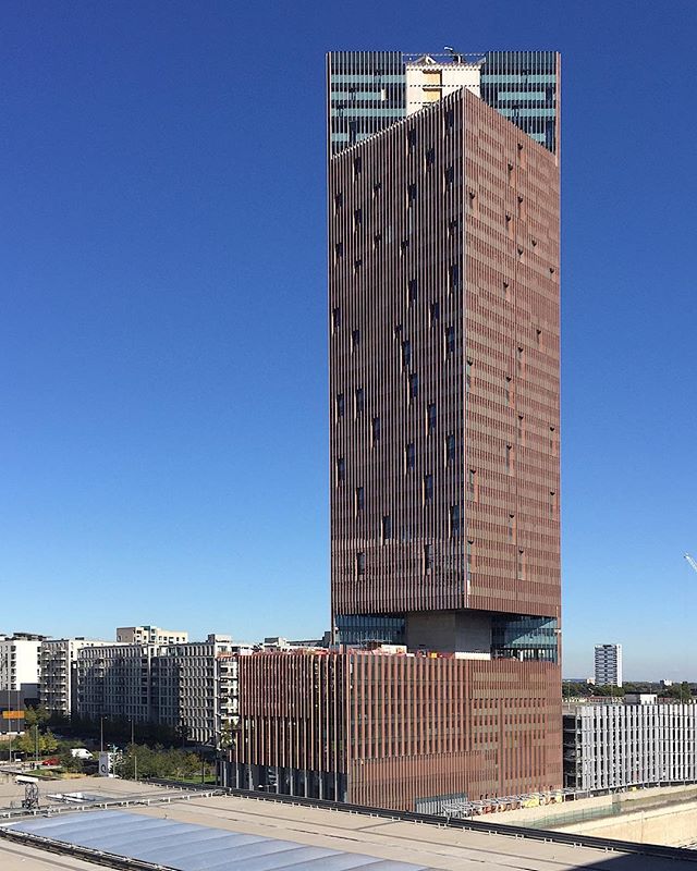 A tall skyscraper stands against a clear blue sky, showcasing modern urban architecture and a vibrant cityscape.