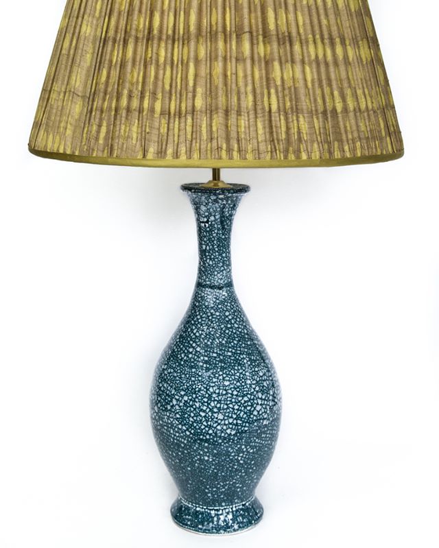 A blue patterned lamp with a golden pleated lampshade on a white background. Great for home decor.