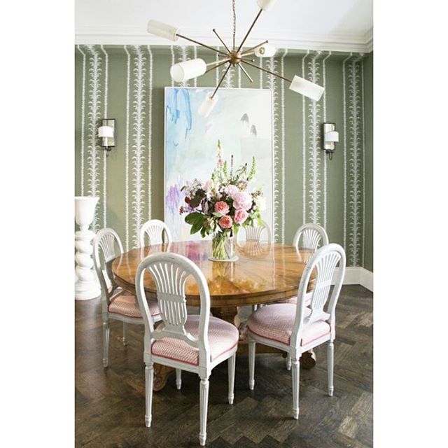 An elegant dining room features a round table surrounded by white chairs under a modern chandelier.