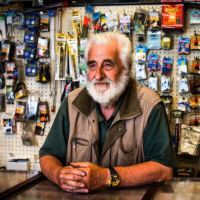 A friendly elderly man with a white beard stands in his store, ready to help customers.