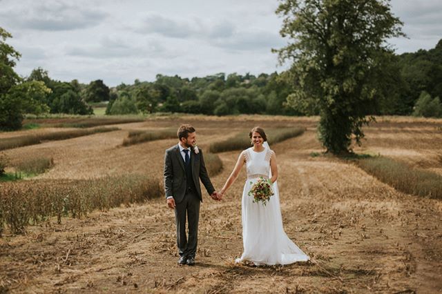 A happy bride and groom hold hands in a rural field on their wedding day, celebrating their love and commitment.