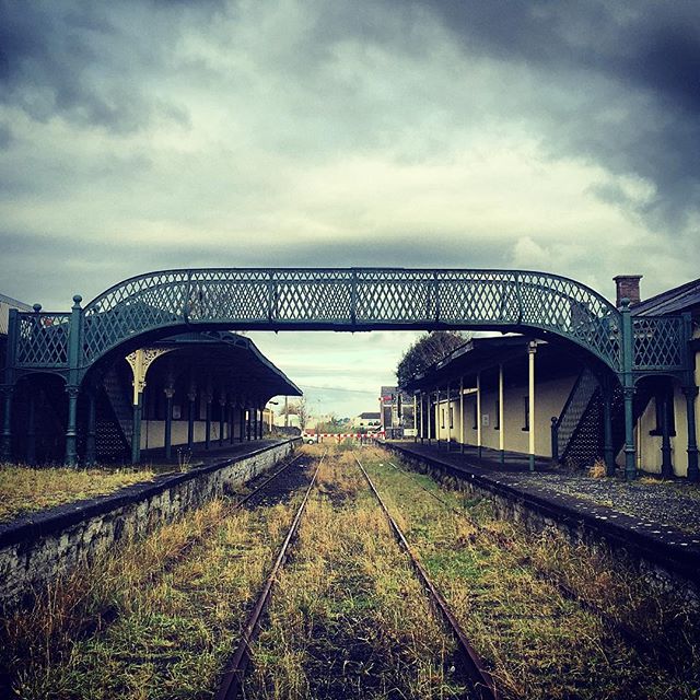 An old train station with overgrown tracks under a cloudy sky gives a sense of mystery and abandonment.