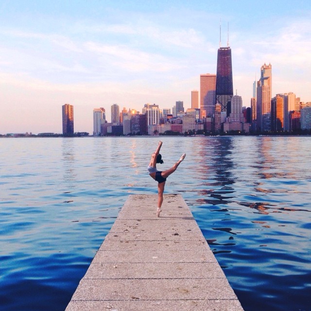 A ballerina dances en pointe on a dock with a stunning city skyline in the background, capturing a peaceful moment.