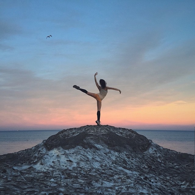 A ballerina poses on a sand dune at sunset, creating a serene and captivating image.