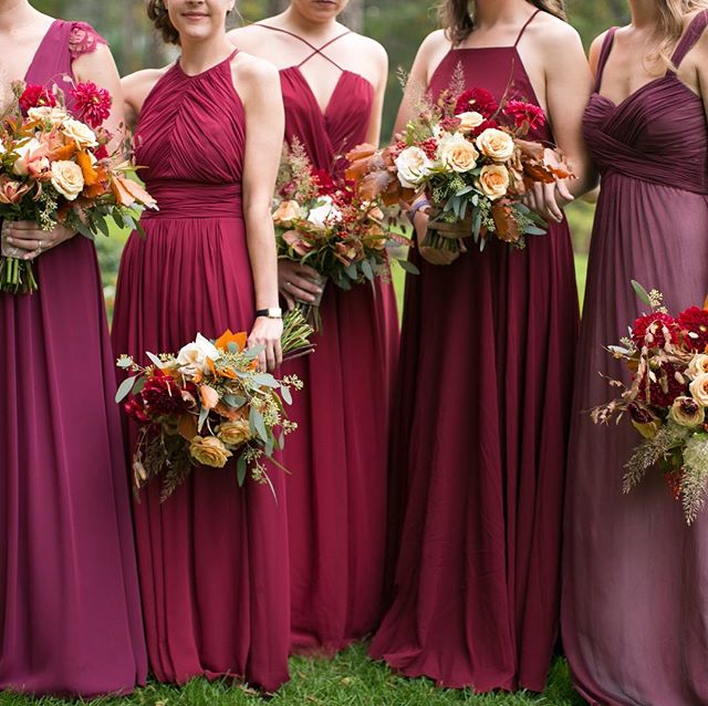 Bridesmaids in maroon dresses hold bouquets at an outdoor wedding, radiating happiness and elegance.