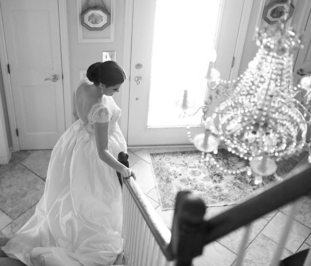 A bride in a white wedding dress descends the stairs, showcasing elegance and classic style.