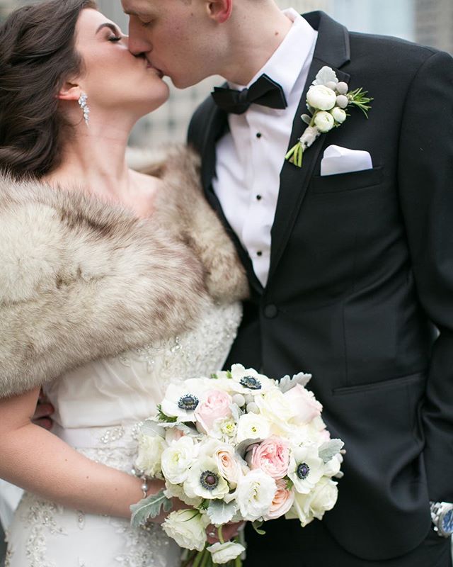 A bride and groom share a kiss while holding a bouquet of flowers on their wedding day.