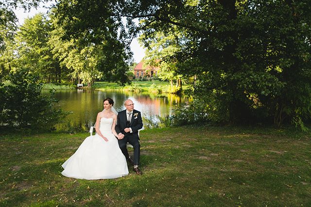 A bride and groom pose by a lake for a wedding photo in a picturesque outdoor setting, showcasing romance.