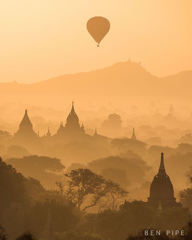 A hot air balloon drifts over the ancient temples of Bagan, Myanmar, at sunrise, shrouded in a golden mist.