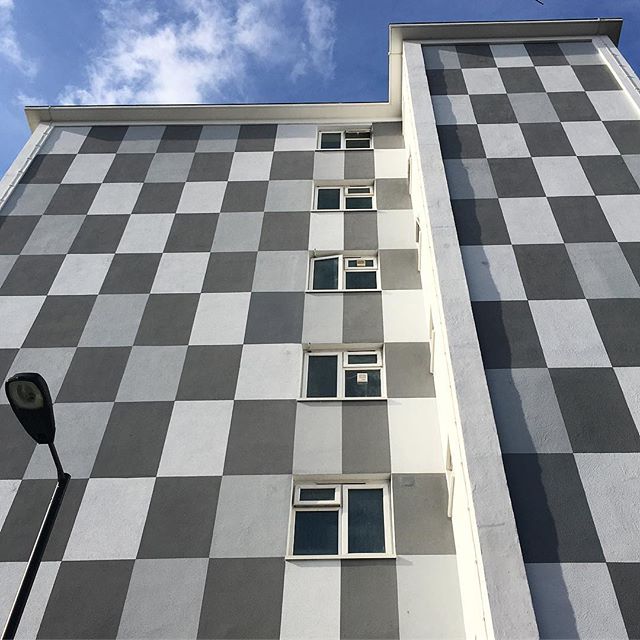 Building facade with checkerboard pattern and windows, captured on a partly cloudy day.
