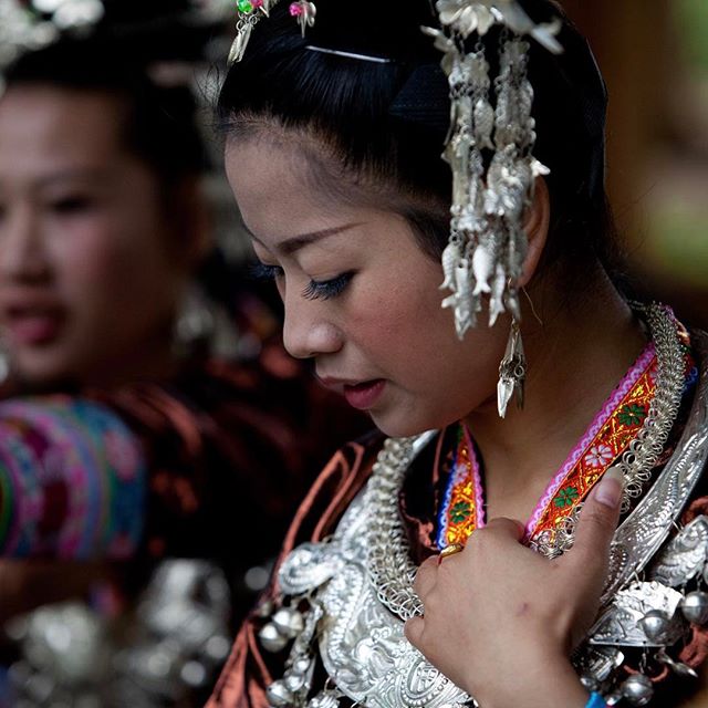 A woman in traditional clothing and silver jewelry is captured in a serene, medium shot outdoors.