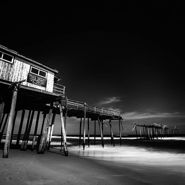 A black and white image showcasing an old pier extending into the ocean, capturing the beauty of coastal architecture.