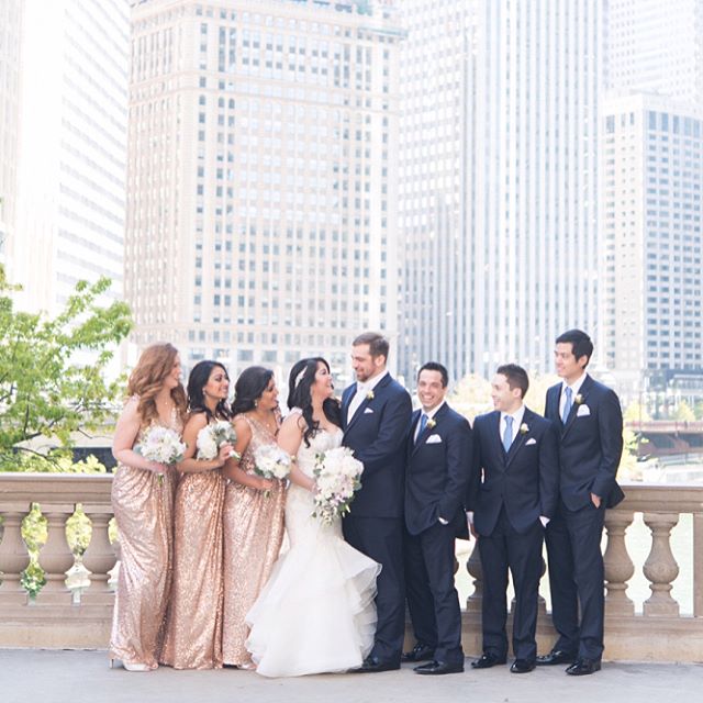 A wedding party poses in front of a cityscape for a classic, modern and elegant picture.
