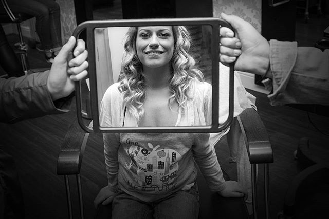 A smiling woman looks into a mirror in a black and white studio shot.