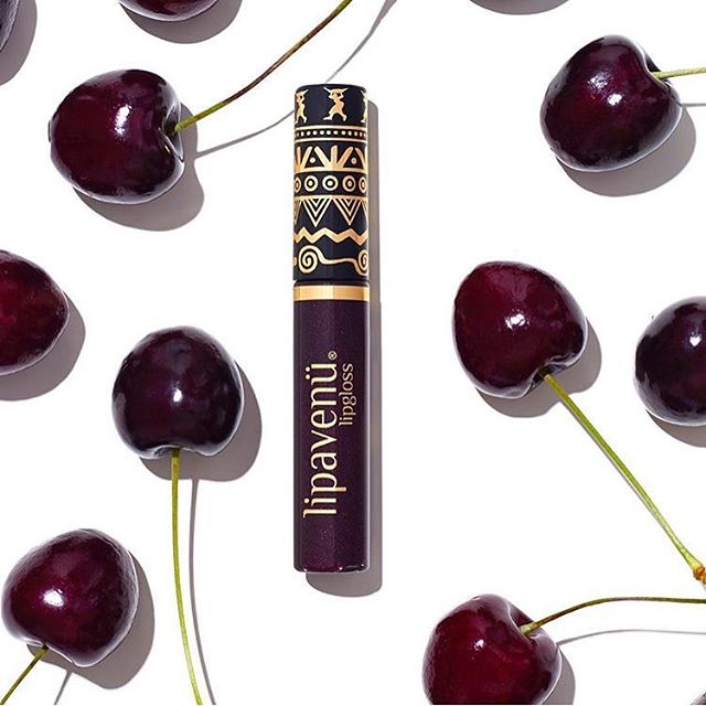A Lipavenu lip gloss sits among fresh, juicy cherries against a clean white backdrop.