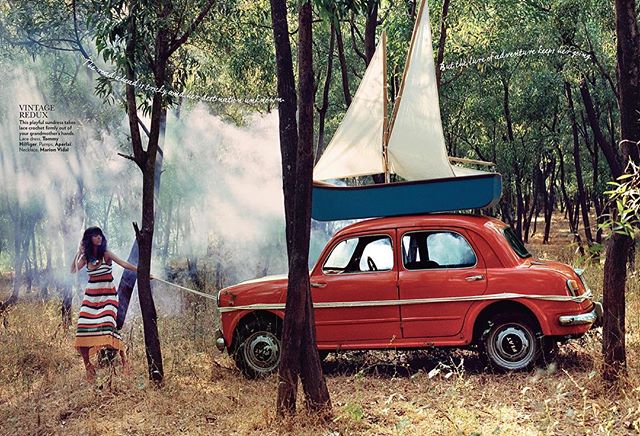 A woman pulls a vintage Fiat with a sailboat on top through a sun-dappled forest, evoking a sense of adventure.