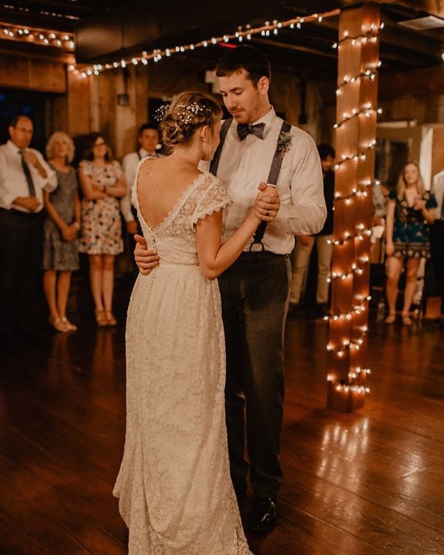 A bride and groom share their first dance at a warmly lit wedding reception surrounded by guests.
