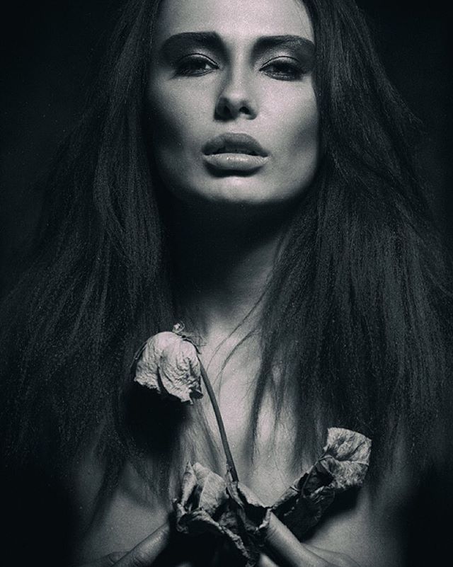 Monochrome portrait of a woman holding a flower in a studio, showcasing emotional intensity and artistic style.