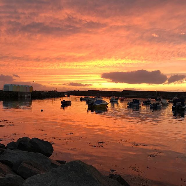 A serene harbor scene with boats at sunset, reflecting warm light across the water.