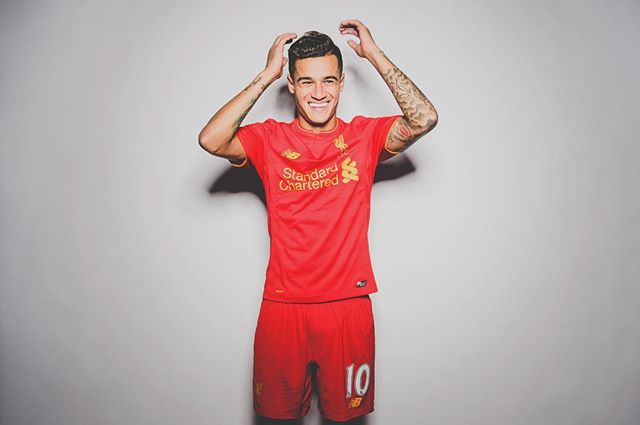 A smiling footballer in red kit poses in a studio setting, representing sports branding and fitness lifestyle.