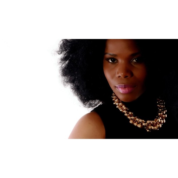 Elegant portrait of a woman with afro hair wearing a gold necklace against a white background.