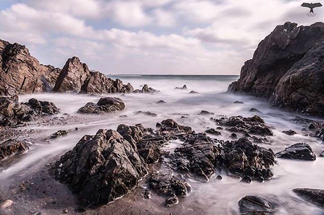 Long exposure capturing the sea washing around rocks on a cloudy day, perfect for travel and nature themes.