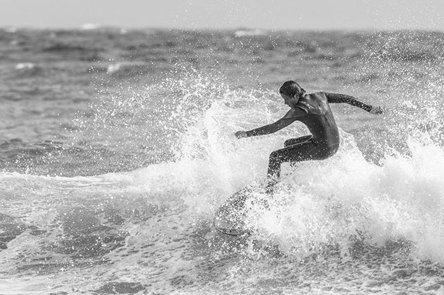 A surfer rides a wave in the ocean, captured in a dynamic black and white shot showcasing action and skill.