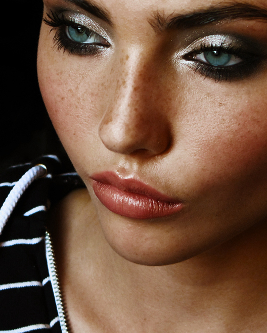 Close-up shot of a woman with freckles and blue eyes wearing glamorous makeup.