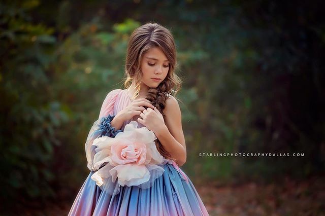 A young girl in a dreamy dress with a flower poses in a soft, natural outdoor setting.