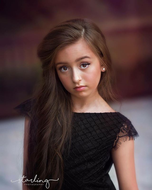 Portrait of a young girl in a black dress, looking directly at the camera with a serious expression.