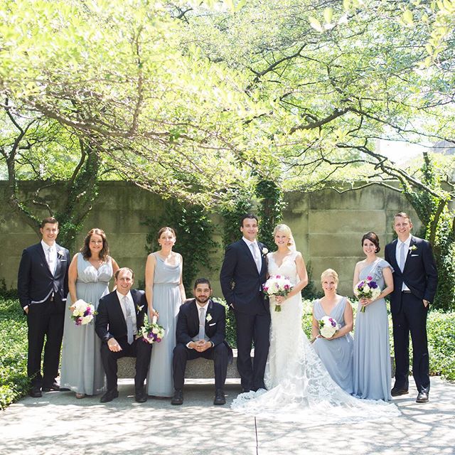A wedding party poses in a garden with the bride and groom in the center.