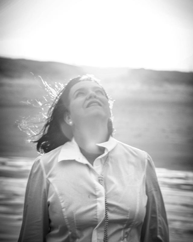 A woman in a white shirt looks up towards the sunlight at the beach, monochrome photo.