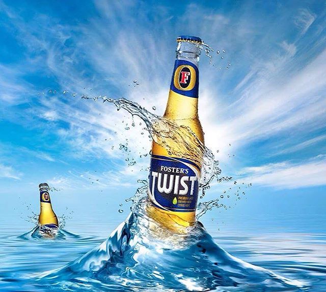 Foster's Twist beer bottles splash in the water under a bright, cloudy blue sky. Refreshing drink advertisement.