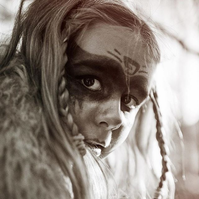 A young girl with face paint and braids stares intensely into the camera in a close-up portrait.