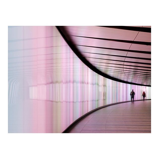 A modern tunnel with pastel lights showcases two people walking towards the light at the end.