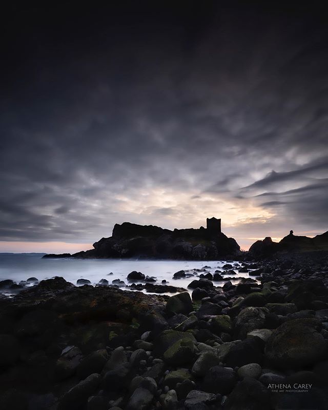 A scenic shot of a castle ruin on a rocky coast under a dramatic sky.