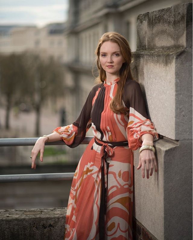 A woman in an elegant dress poses in an outdoor urban setting, creating a sophisticated portrait.