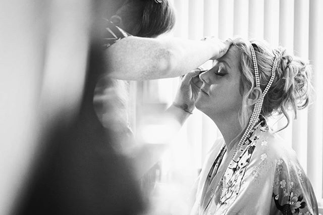 A bride is getting her makeup done by a makeup artist in preparation for her wedding day.