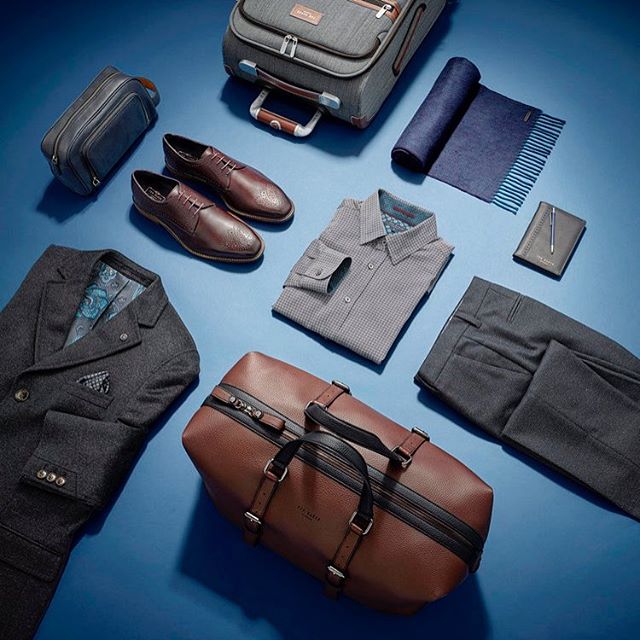 Elegant men's travel essentials including suit, shirt, luggage, and leather accessories on a blue background.