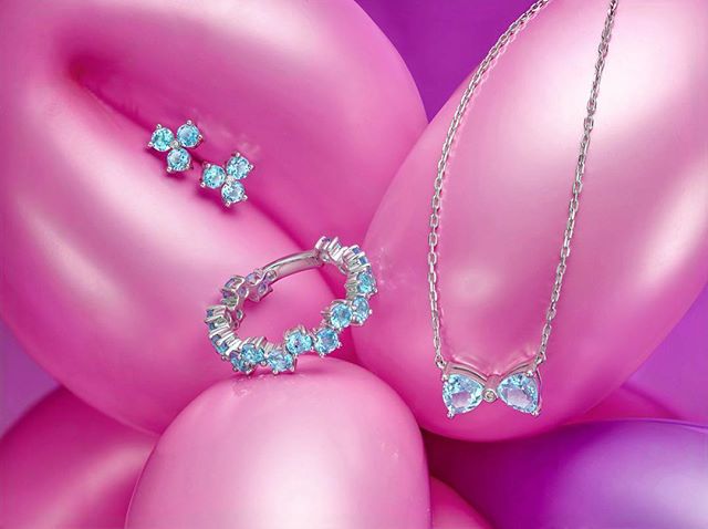 Elegant jewelry set featuring earrings, a ring, and a necklace with blue stones on a soft pink background. Perfect for gifting.
