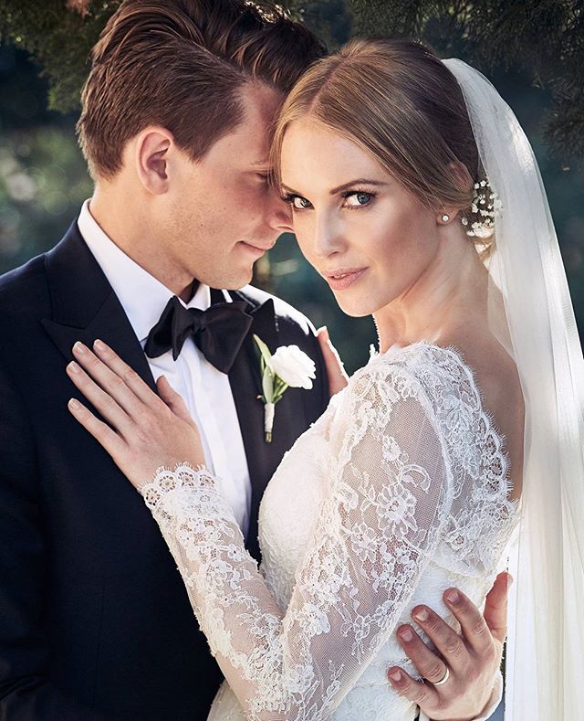 An elegant couple embrace on their wedding day, the bride in lace and veil, the groom in a classic tuxedo.