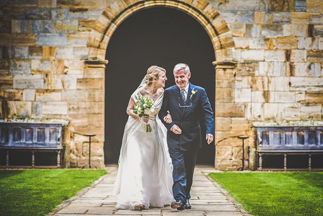A bride and her father walking on a path in front of a church on her wedding day.