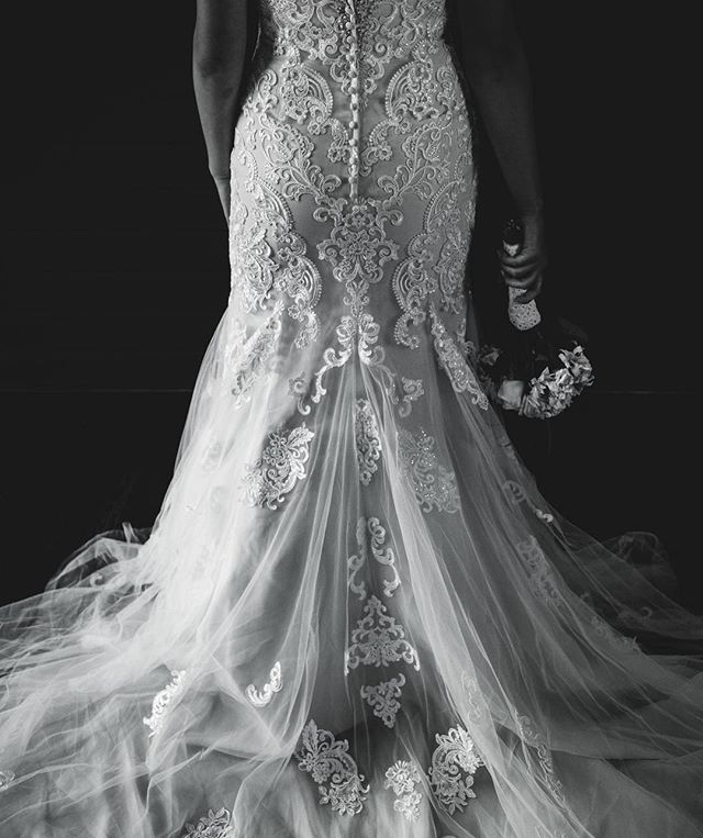 A bride from behind showcases her elegant lace wedding dress and bouquet.