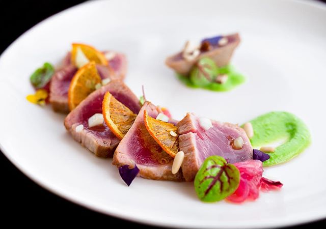 A beautifully plated dish of tuna with orange slices and green sauce on a white plate, perfect for food blogs and restaurant marketing.