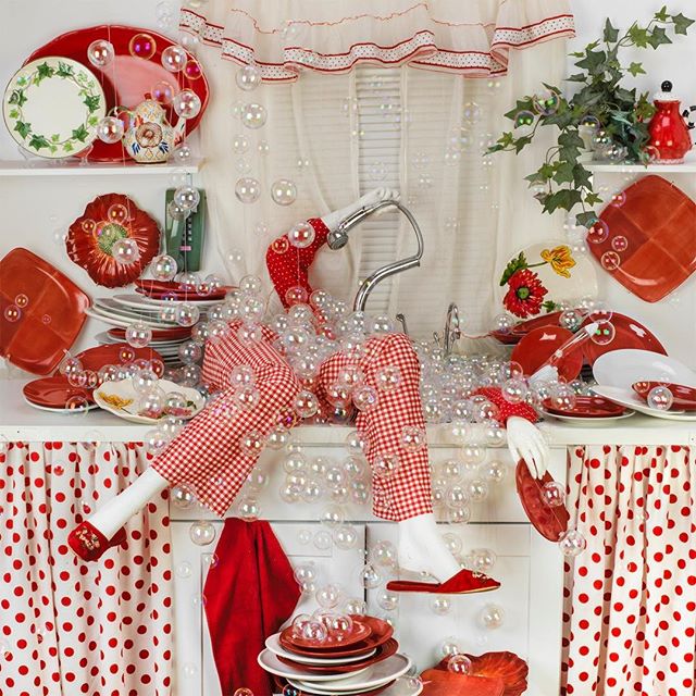A whimsical kitchen scene filled with red and white dishes and bubbles, evokes a dreamy, playful atmosphere.