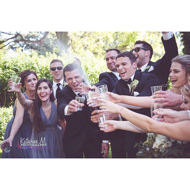 A joyous wedding party celebrates with a champagne toast in a lush garden setting.