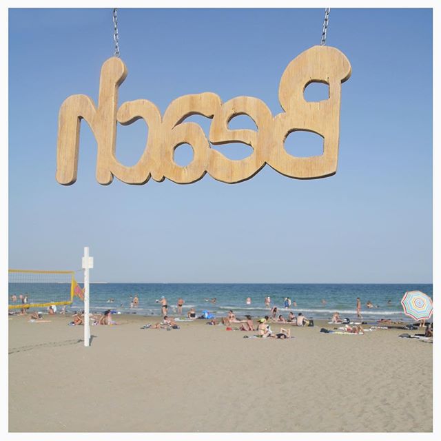 A sunny day at the beach with people relaxing under a wooden 'Beach' sign.
