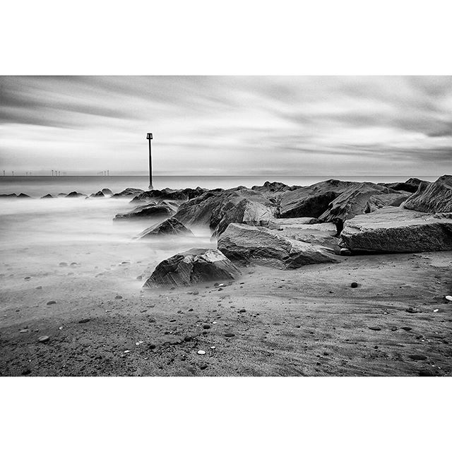 A black and white seascape featuring rocks and a post on a serene beach, perfect for travel or background use.