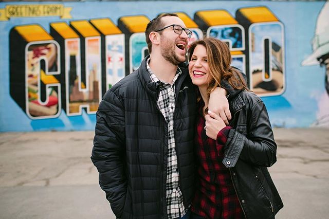 A happy couple laughs and embraces in front of a Chicago mural, showcasing a fun and loving moment.
